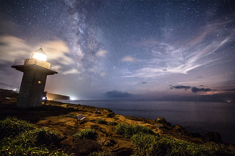 星が輝く夜、灯台が光を放つ幻想的な情景